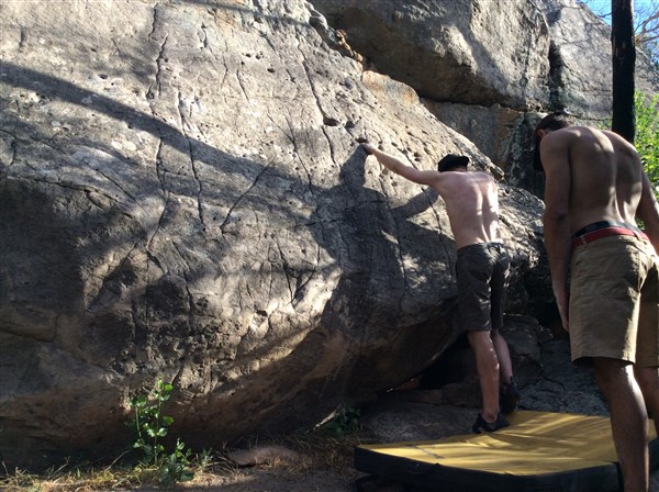 Giles Short rock climbing wearing shorts, hat and grippy shoes stood on crash mat