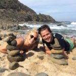 Blonde girl and brunette guy laying on beach with pebble towers