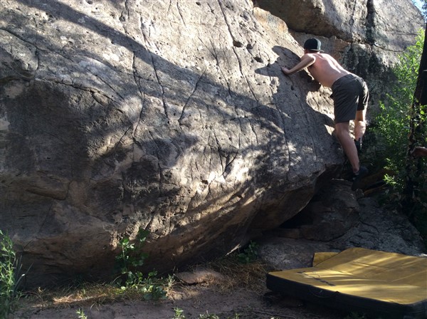 Giles Short rock climbing wearing shorts, hat and grippy shoes with crash mat underneath