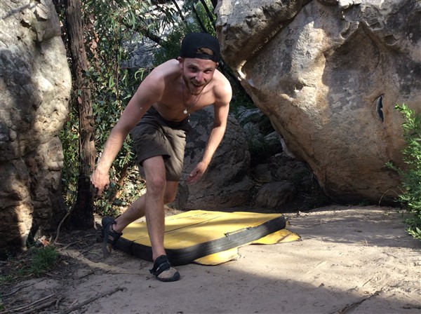 Giles Short wearing shorts, hat and grippy shoes with crash mat standing back up after climb