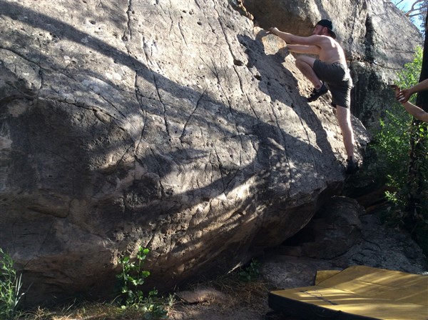 Giles Short rock climbing wearing shorts, hat and grippy shoes with crash mat underneath