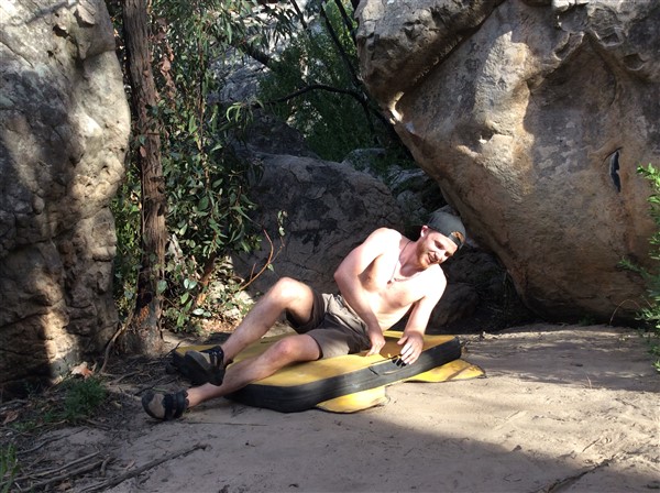 Giles Short wearing shorts, hat and grippy shoes laying on crash mat after climb