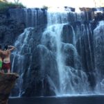 Giles Short saluting with swim shorts below bum with friend in front of waterfall