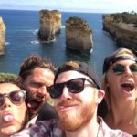 Giles Short selfie tongues out with 2 girls and 1 guy in front of rock coast formation