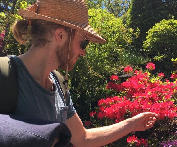 Giles Short wearing straw hat and sunglasses touching red flowers