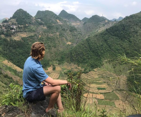 Giles Short sitting on edge of steep slope with rice terrace below