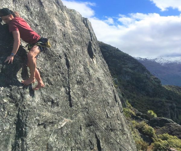 Giles Short rock-climbing barefoot on cliff next to mountain